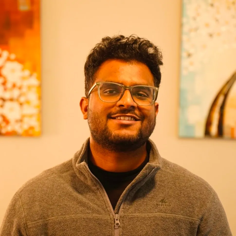Kalyan Chandana, smiling, in front of two paintings